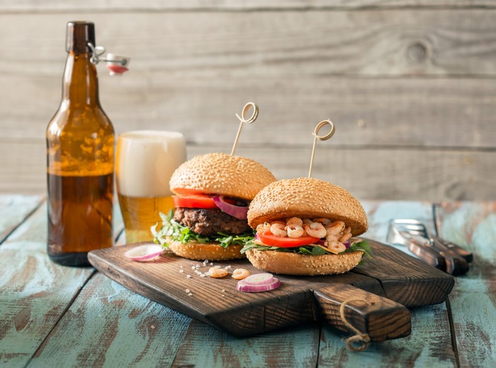 Two gourmet burgers and a beer bottle