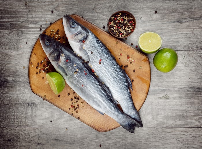 Two raw fish with limes and peppercorns on a cutting board