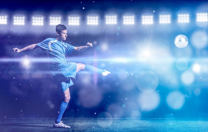 Man in blue uniform kicking soccer ball on stadium