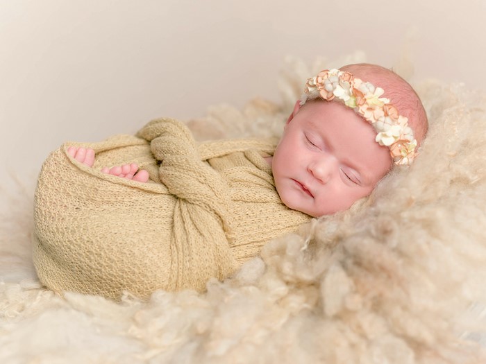 Newborn baby girl sleeping wrapped in a blanket with a flower crown