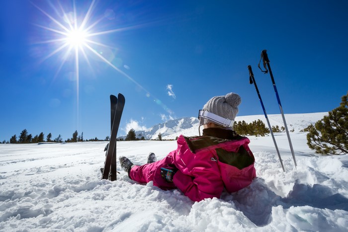 Woman in pink jacket relaxing in snow with skis