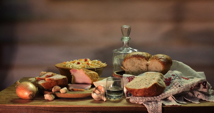 Still life with vodka, bread, ham, and vegetables