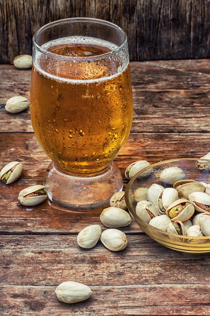 Glass of beer with pistachios on wooden table