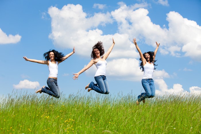 Three women jumping in a grassy field under a blue sky