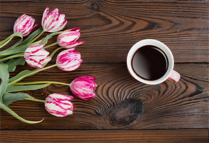 Pink and white tulips with a cup of coffee on a wooden table