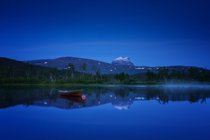 Boat on a calm lake with mountains at night