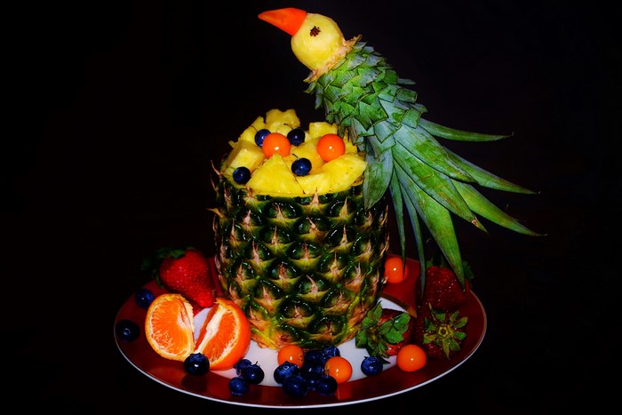 Pineapple carved into a parrot with fruit on a plate