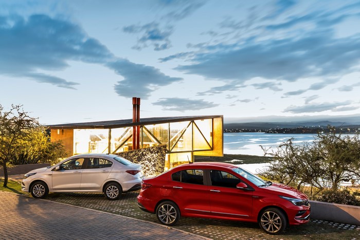 Two Fiat Cronos cars parked near a modern house by a lake