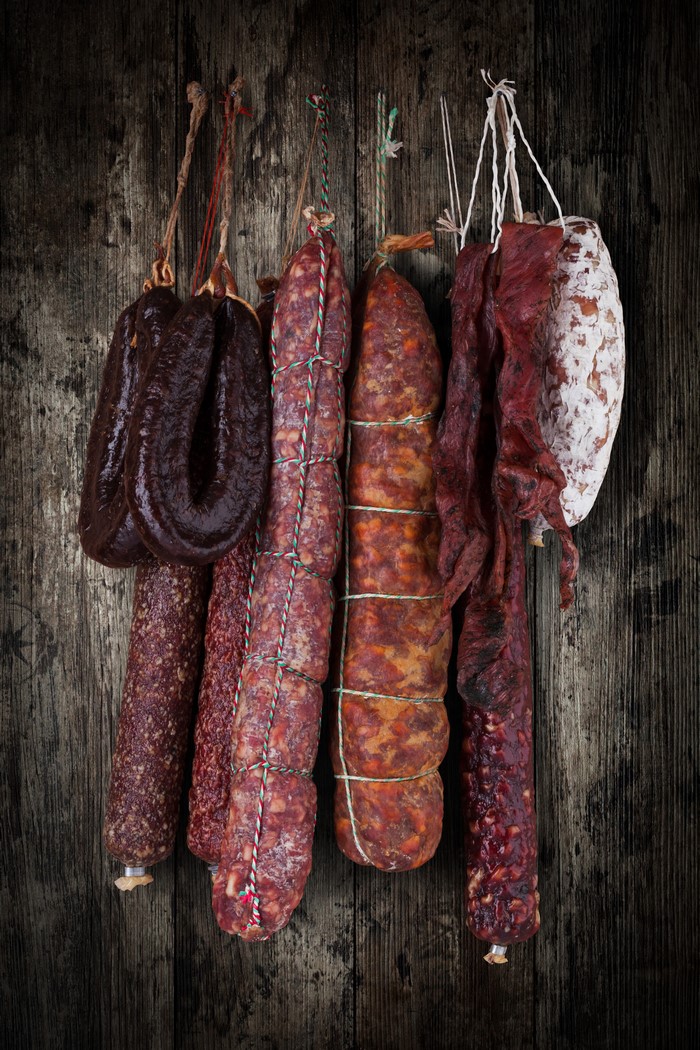 Various cured sausages hanging on a wooden background