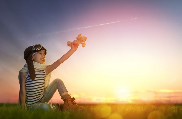 Girl in pilot hat holding toy airplane at sunset