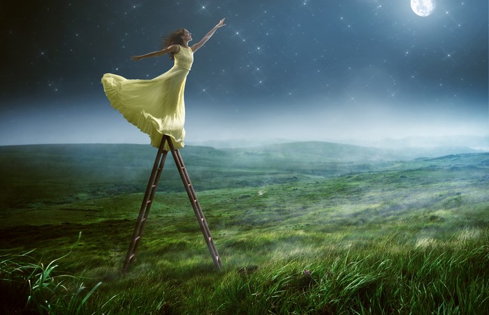 Woman in yellow dress on ladder reaching for moon