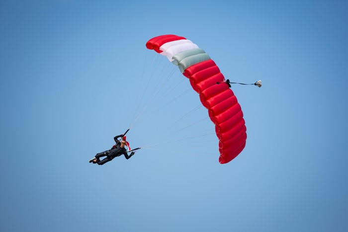 Skydiver with red and white parachute against blue sky