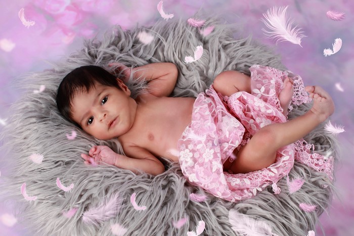 Newborn baby lying on fluffy rug with pink feathers