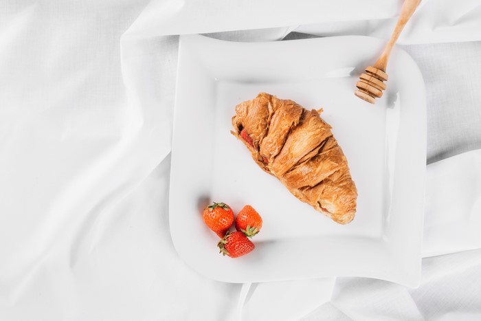 Croissant with strawberries and honey dipper