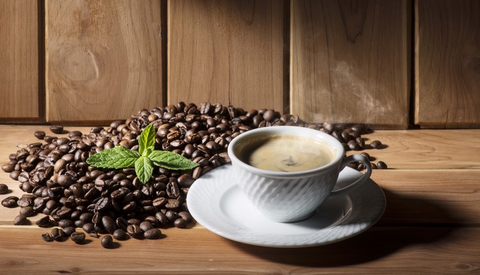 Coffee beans, cup of coffee, and mint on wood
