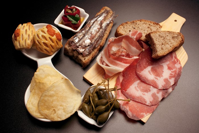 Charcuterie board with anchovies, ham, bread, and chips