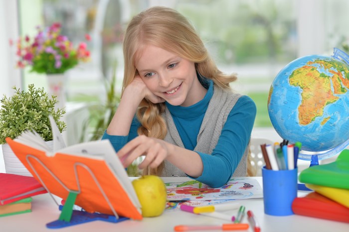 Girl reading a book with a globe on the table