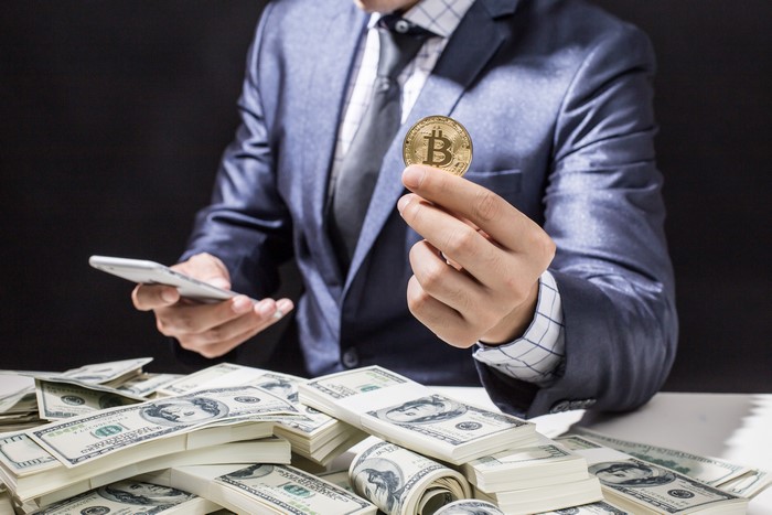 Man in Suit Holding Bitcoin and Smartphone with Dollars