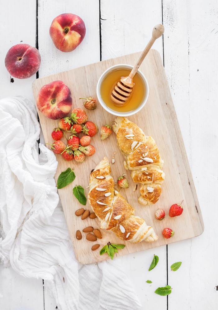 Croissants with peaches, strawberries, honey, and almonds on a cutting board