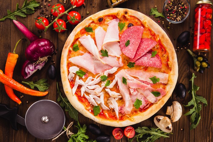 Pizza with Ham, Sausage, and Vegetables on Wooden Table
