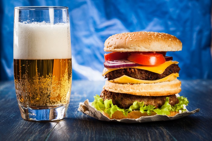 Beer and a double hamburger with lettuce, tomato, onion, and cheese