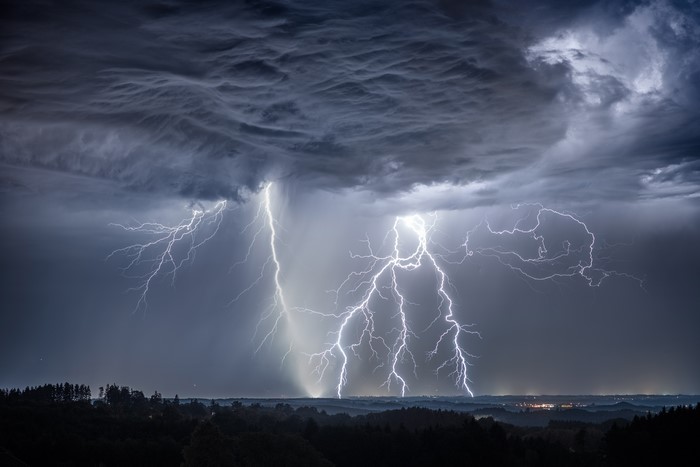 Lightning strikes through thunderclouds over a landscape