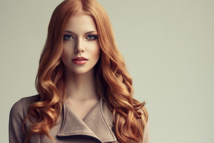 Redhead woman with wavy hair wearing a beige jacket
