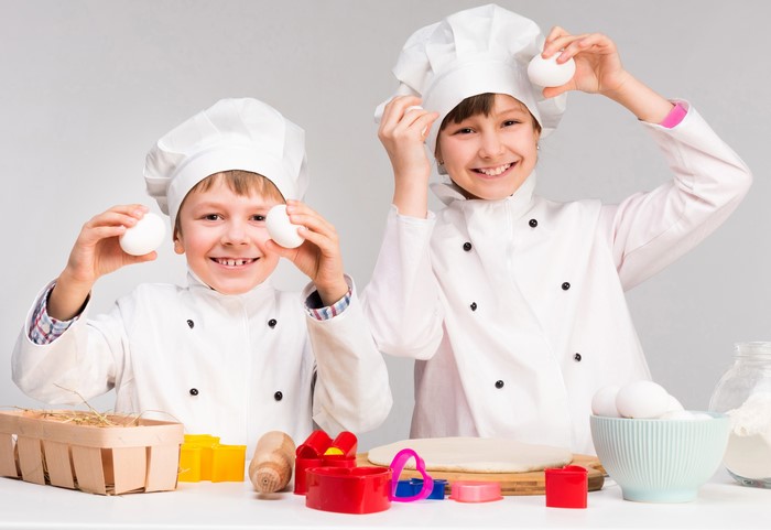 Two children in chef hats holding eggs