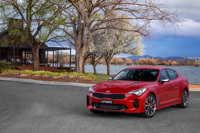 Red Kia Stinger parked by a lake and house