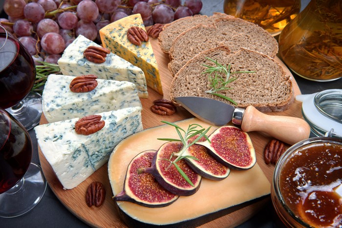 Cheese board with grapes, bread, figs, nuts, and wine