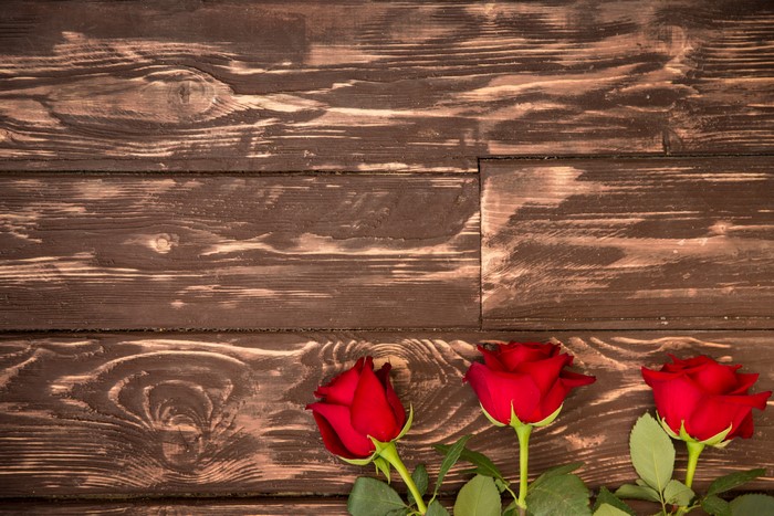 Three red roses on a wooden background