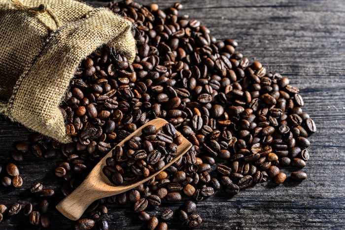 Coffee beans spilling from a burlap sack onto a wooden surface
