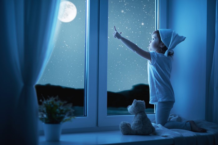 Little girl looking at the moon and stars through a window