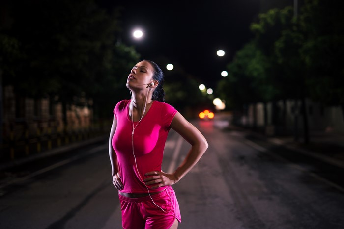 Woman in pink workout clothes with headphones at night