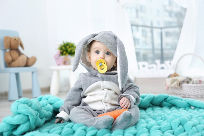 Baby in a bunny costume with a pacifier and carrot