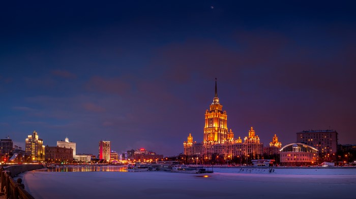 Moscow skyline with illuminated buildings and frozen river at dusk