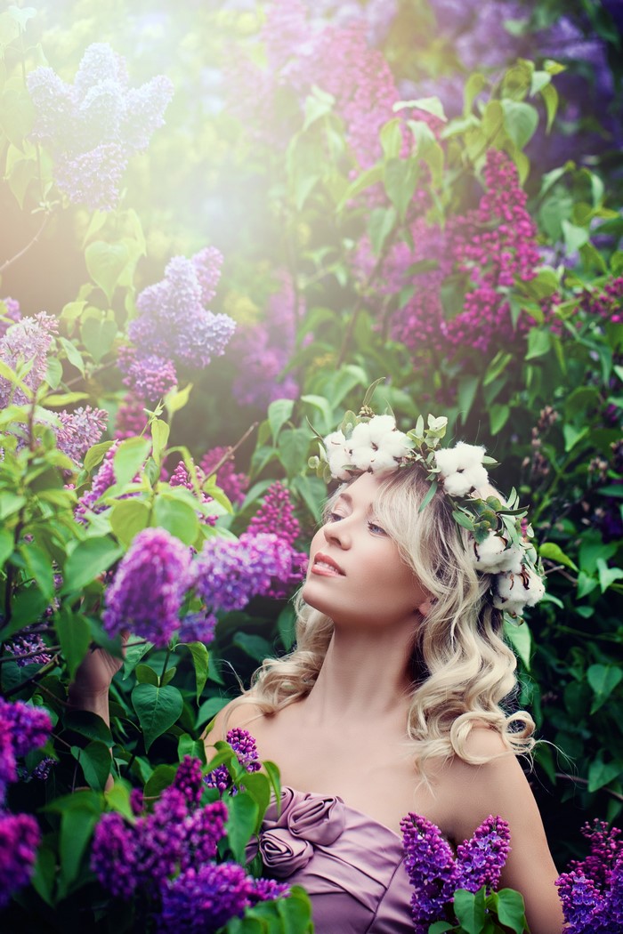 Blonde girl with flower crown in lilac bushes
