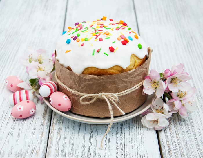 Easter cake with decorated eggs and flowers on wooden background