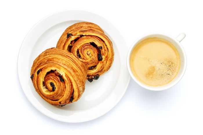 Two raisin buns on a plate with a cup of coffee