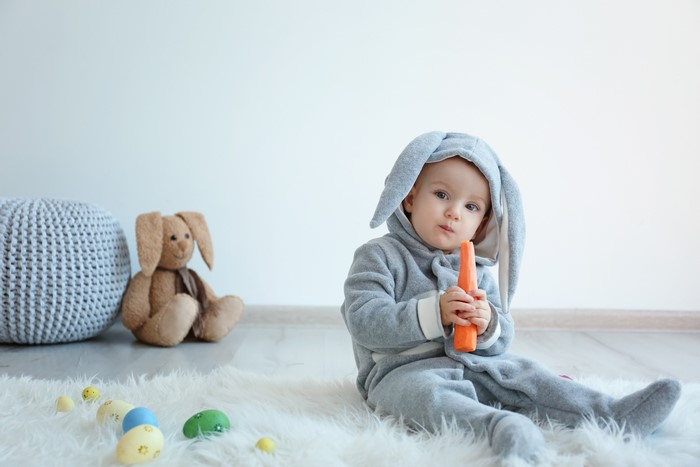 Baby in bunny costume holding carrot with Easter eggs