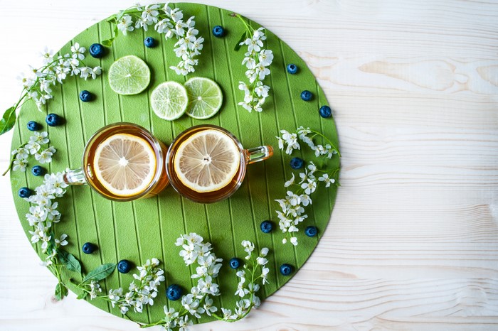 Two cups of tea with lemon slices, blueberries, and white flowers