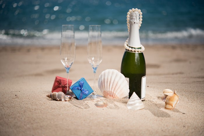 Champagne bottle and glasses on a beach with gifts and shells