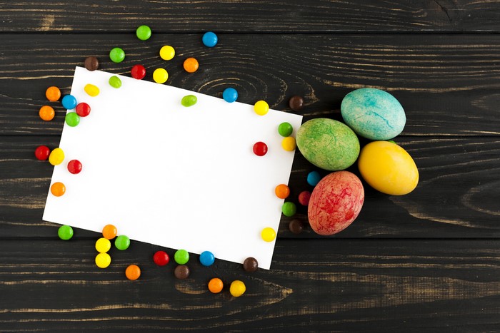 Easter eggs and candies on a wooden background with a blank card