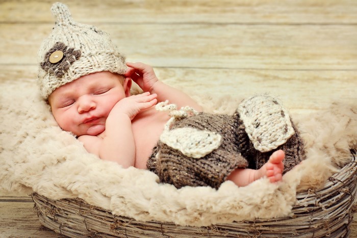 Newborn baby sleeping in a basket wearing a winter hat