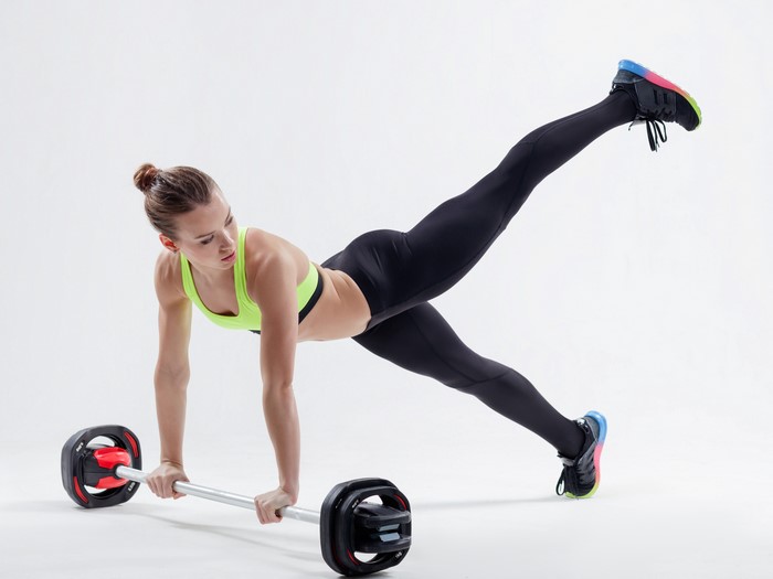 Woman performing a plank with a barbell and leg lift
