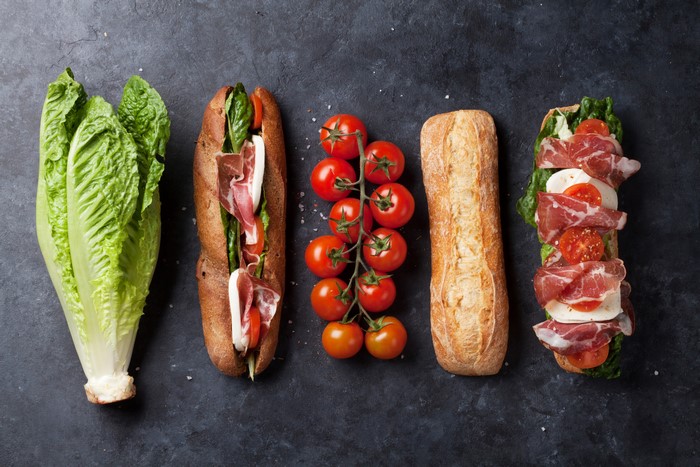Sandwich ingredients and prepared sandwiches on dark background