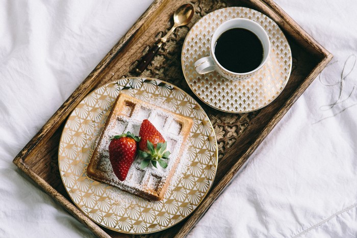 Waffle with strawberries and coffee on a tray