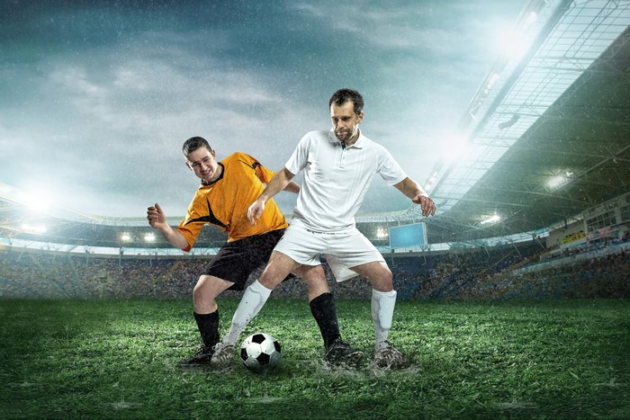 Two male soccer players in the rain on a stadium field