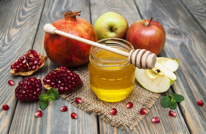 Honey jar with pomegranates and apples on wood