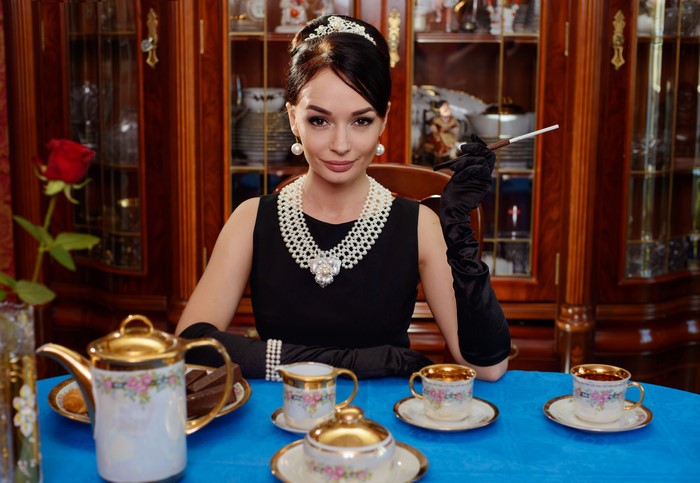 Woman in black dress with pearls and tiara holding cigarette holder